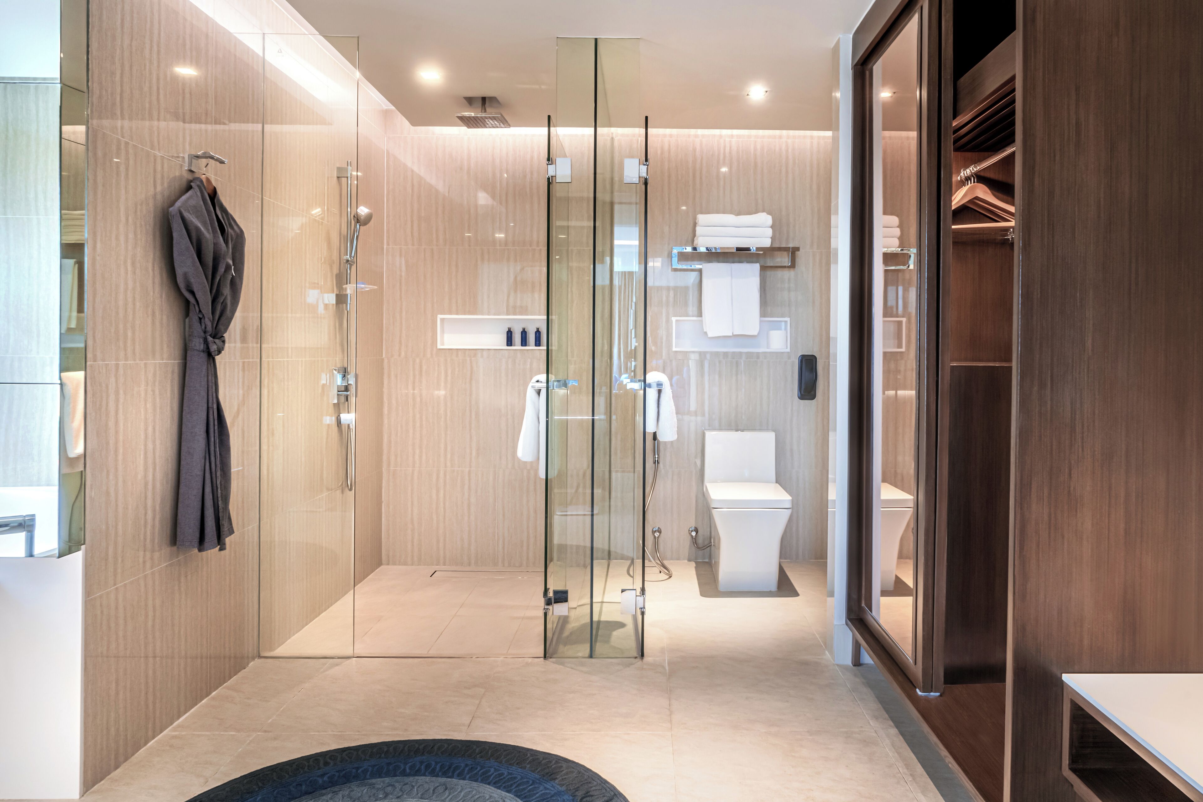 A modern bathroom with a glass shower enclosure, a toilet, and a walk-in closet with shelves.