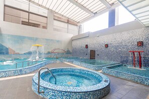 An indoor swimming pool with multiple sections, including a central hot tub and smaller pools, surrounded by tiled walls and a high ceiling with skylights. - Kilin Hotel, JiaoXi (Jiaoxi)