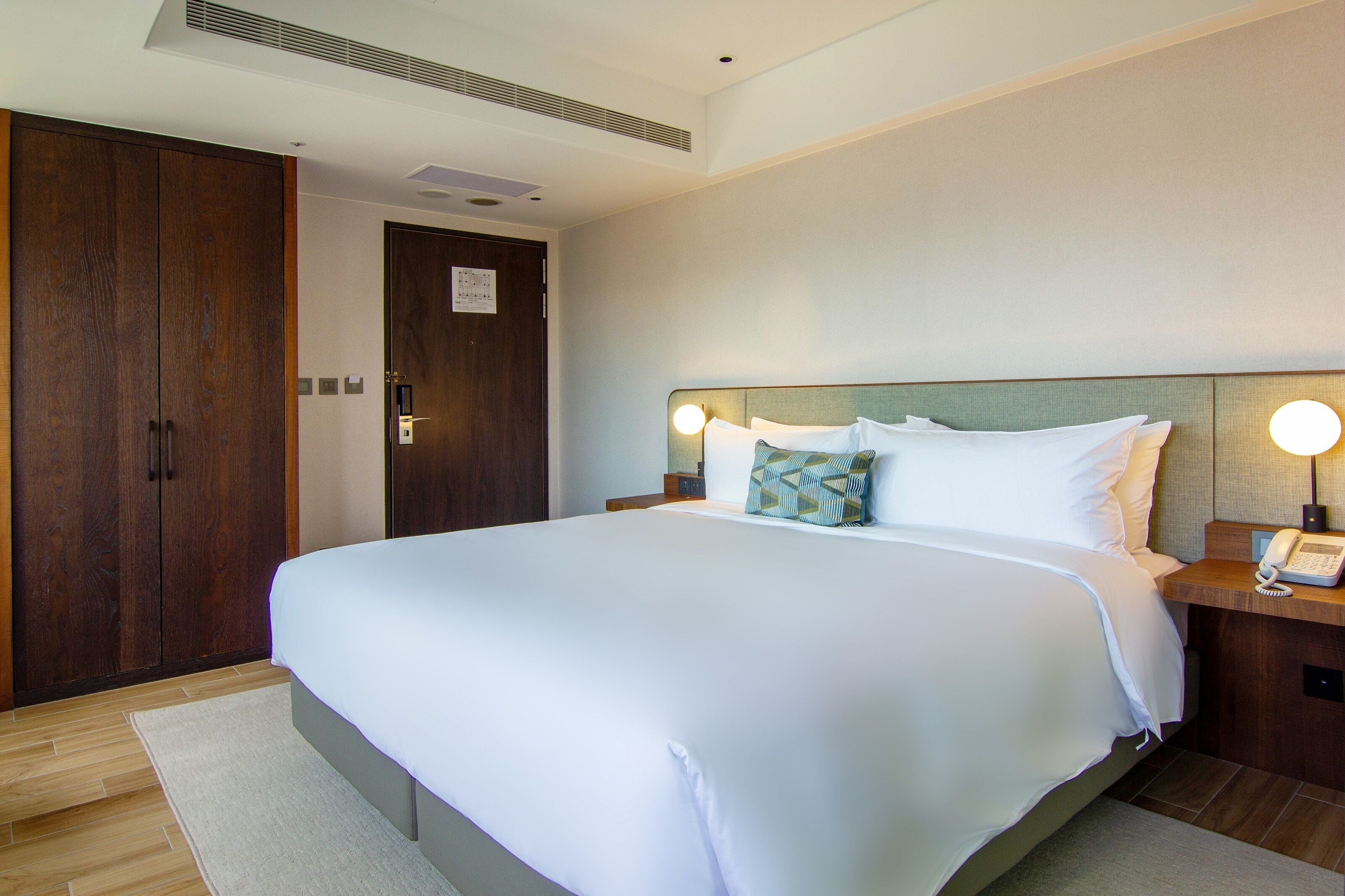 A hotel room with a large bed, wooden wardrobe, bedside lamps, and a telephone on the nightstand.