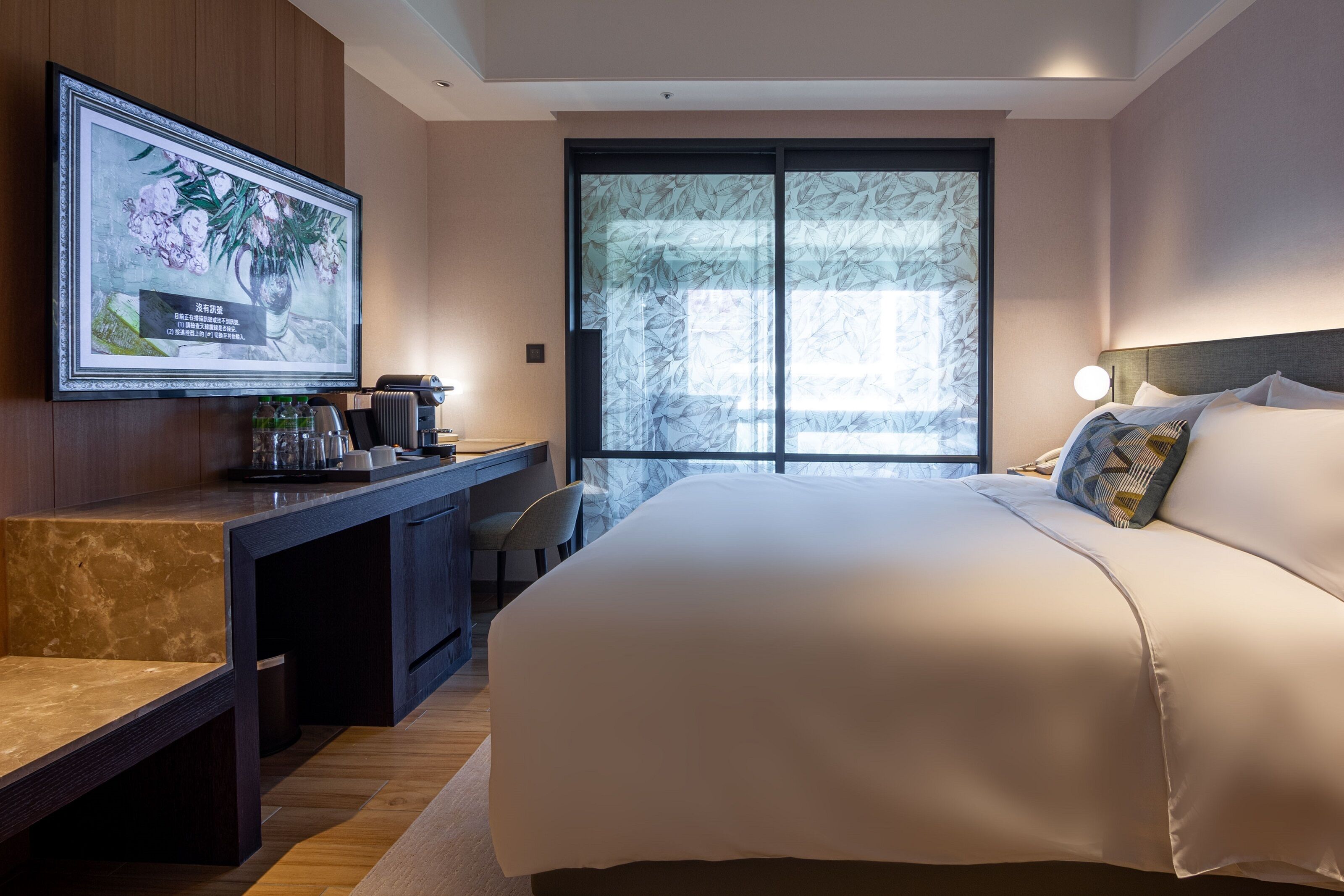 Habitación de hotel moderna con una cama grande, un escritorio con silla, televisión montada en la pared y un ventanal con vistas.
