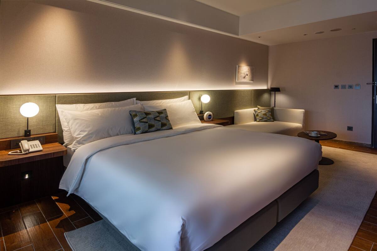 Ein modernes Hotelzimmer mit einem großen Bett, Nachttischlampen, einem Telefon auf dem Nachttisch und einem kleinen Tisch mit einer Tasse.