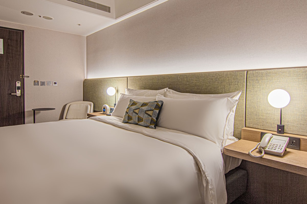 Ein Hotelzimmer mit einem großen Bett, Nachttischlampen, einem Telefon und einem kleinen Tisch.