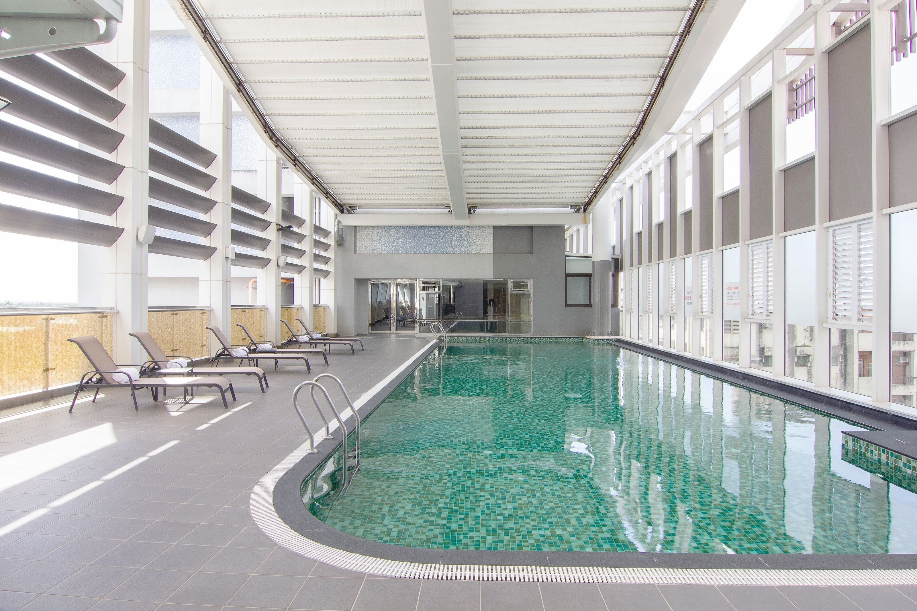 An indoor swimming pool with clear water, sun loungers, and a tiled floor.