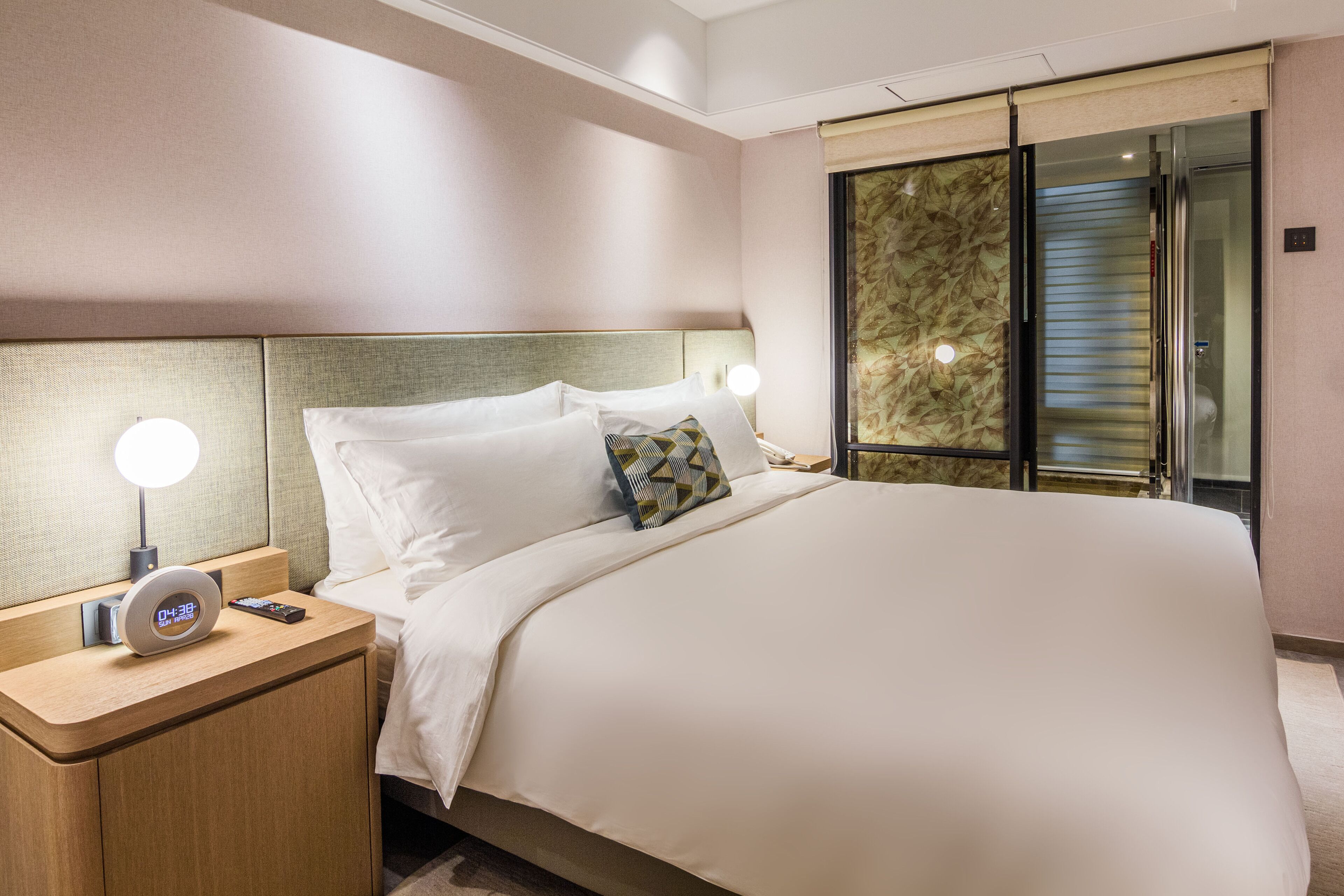 A hotel room with a large bed, a bedside table with a lamp, and a clock.