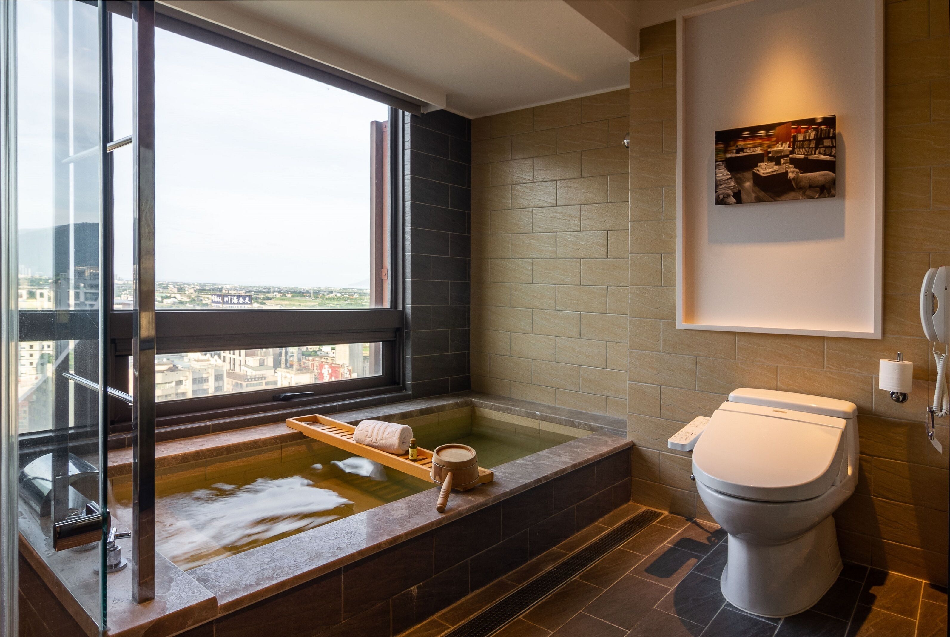 A modern bathroom with a large window, a bathtub, and a toilet.