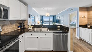 A modern kitchen with white cabinets, a stainless steel dishwasher, and a black countertop.