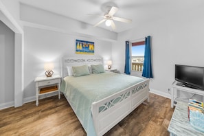 A bedroom with a bed, a ceiling fan, a TV, and a window with curtains.