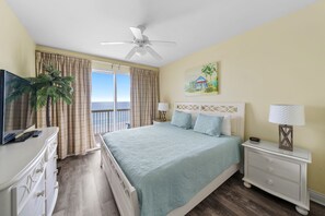 Habitación de hotel con cama, televisor, escritorio y balcón con vista al océano.