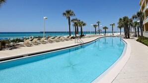 A swimming pool with lounge chairs and palm trees, overlooking a beach and ocean.