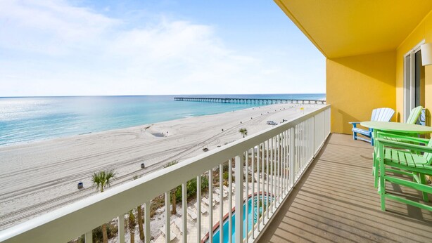 A balcony with a view of a beach, a pier, and a swimming pool.