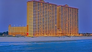 A large, multi-story hotel with a red roof, located near a beach.