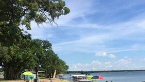 Ein Strand mit einer Rasenfläche, einigen Sonnenschirmen und einem Gewässer im Hintergrund.