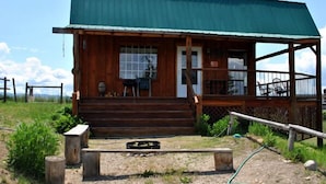 A wooden cabin with a green roof, a porch with chairs, and a small garden area. - Wilderness Spirit Cabins, LLC-'Eagle Nest'- Heavenly Mountain Views (Corvallis)