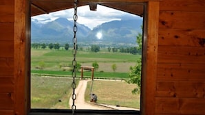 A wooden cabin with a large window overlooking a rural landscape with mountains and a dirt path. - Wilderness Spirit Cabins, LLC-'Eagle Nest'- Heavenly Mountain Views (Corvallis)