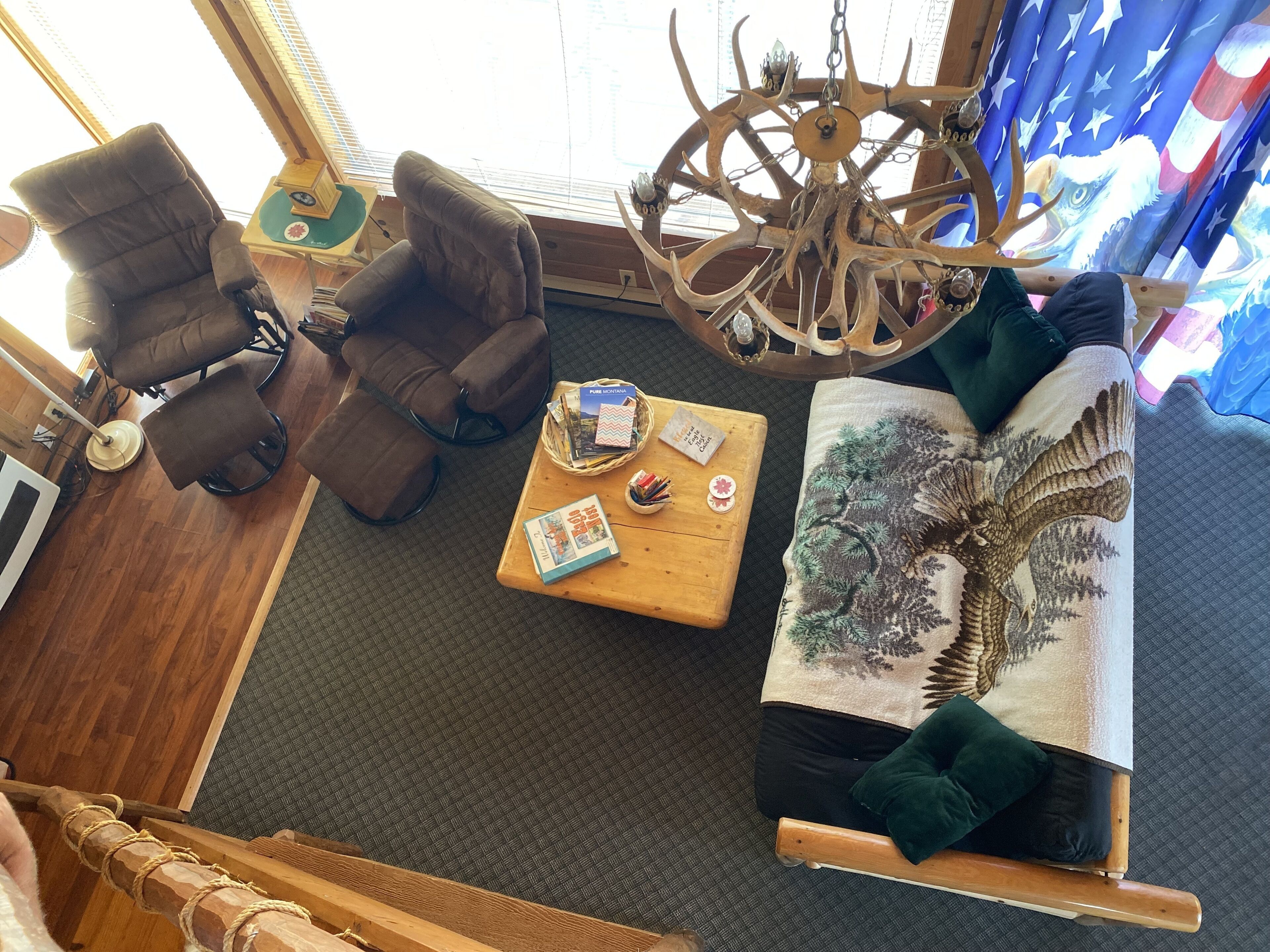 A room with a large wooden chair, a small table with books and a decorative item, and a large tapestry with an eagle design.