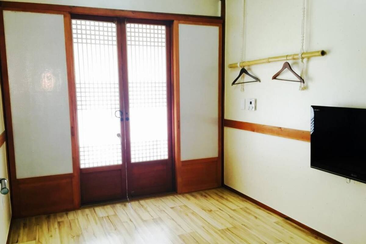A room with wooden flooring, a sliding door with a grid pattern, a wall-mounted TV, and two hangers on a rod.