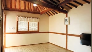 A room with wooden beams on the ceiling, a window with a lattice design, and a wall-mounted TV. - Hanok Raon (Gyeongju)