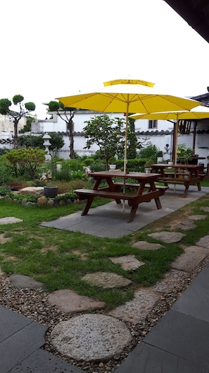 A garden patio with wooden picnic tables and yellow umbrellas. - Hanok Raon (Gyeongju)