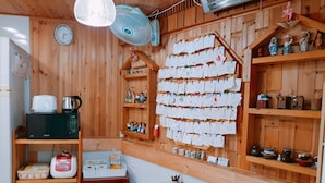 A cozy room with wooden walls, a wooden table, a microwave, a kettle, and shelves with various items. - Hanok Raon (Gyeongju)