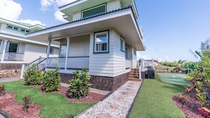 A two-story house with a balcony, a stone foundation, and a well-maintained lawn with a putting green.