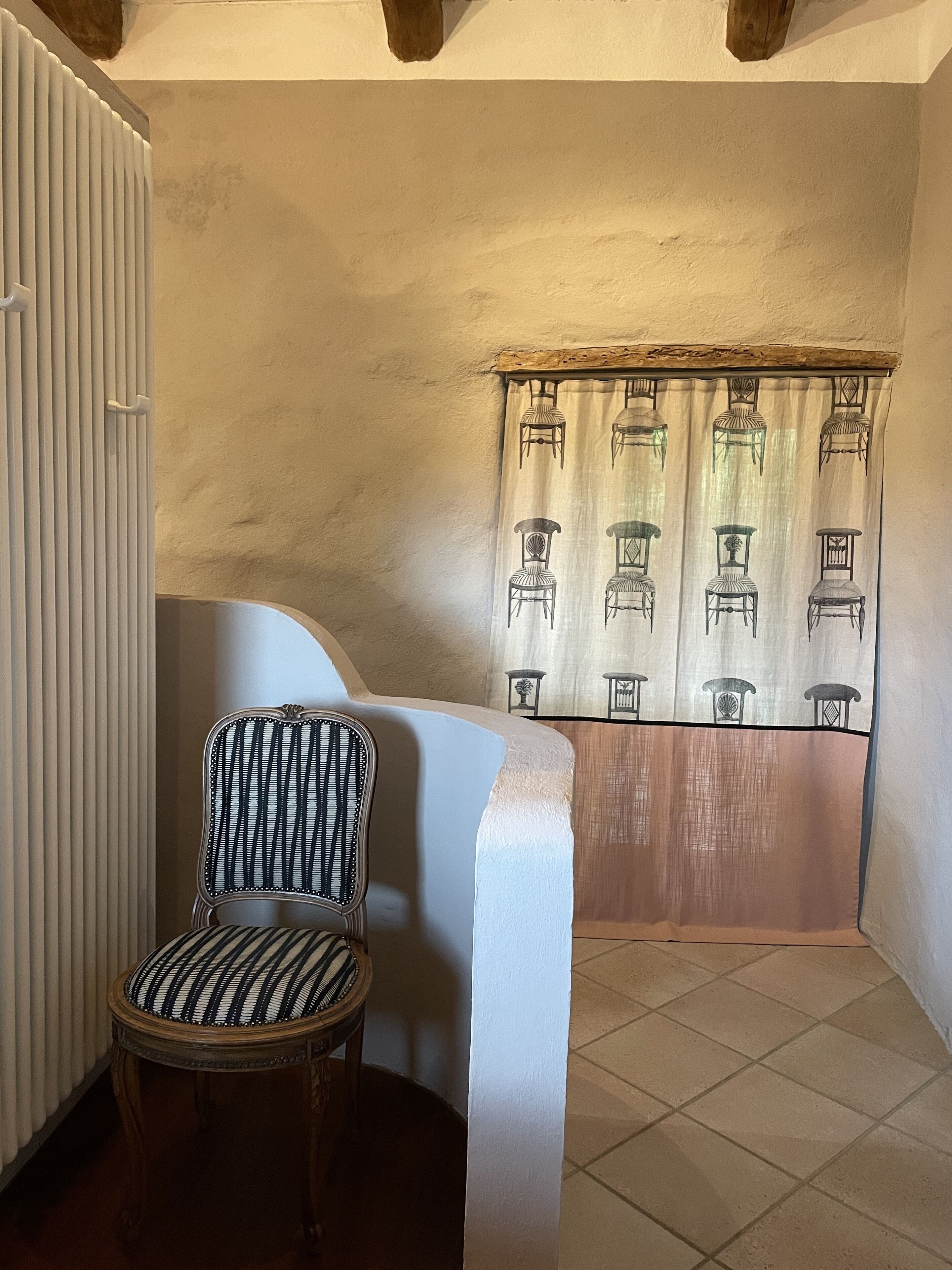 Une pièce d’angle avec un radiateur, une chaise et une fenêtre ornée de rideaux à motifs.
