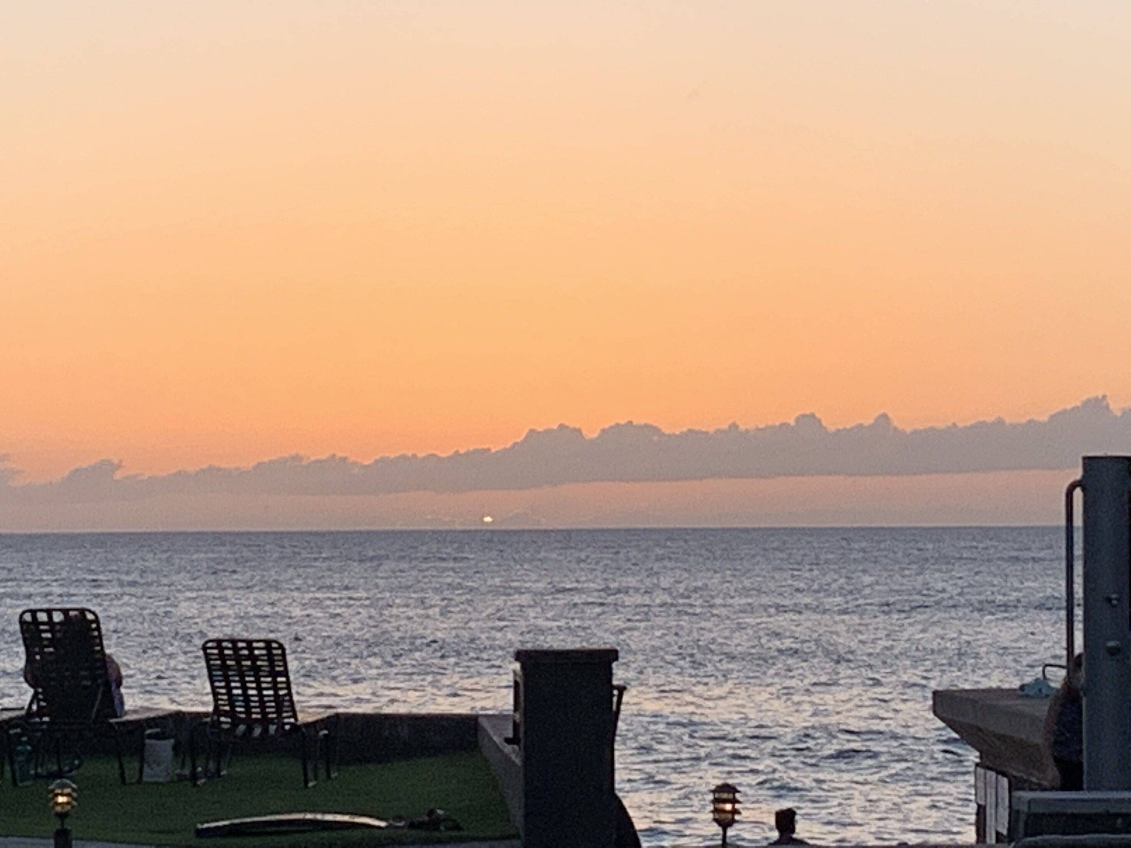 Eine Strandterrasse mit Stühlen und einer Laterne, mit Blick auf den Ozean bei Sonnenuntergang.