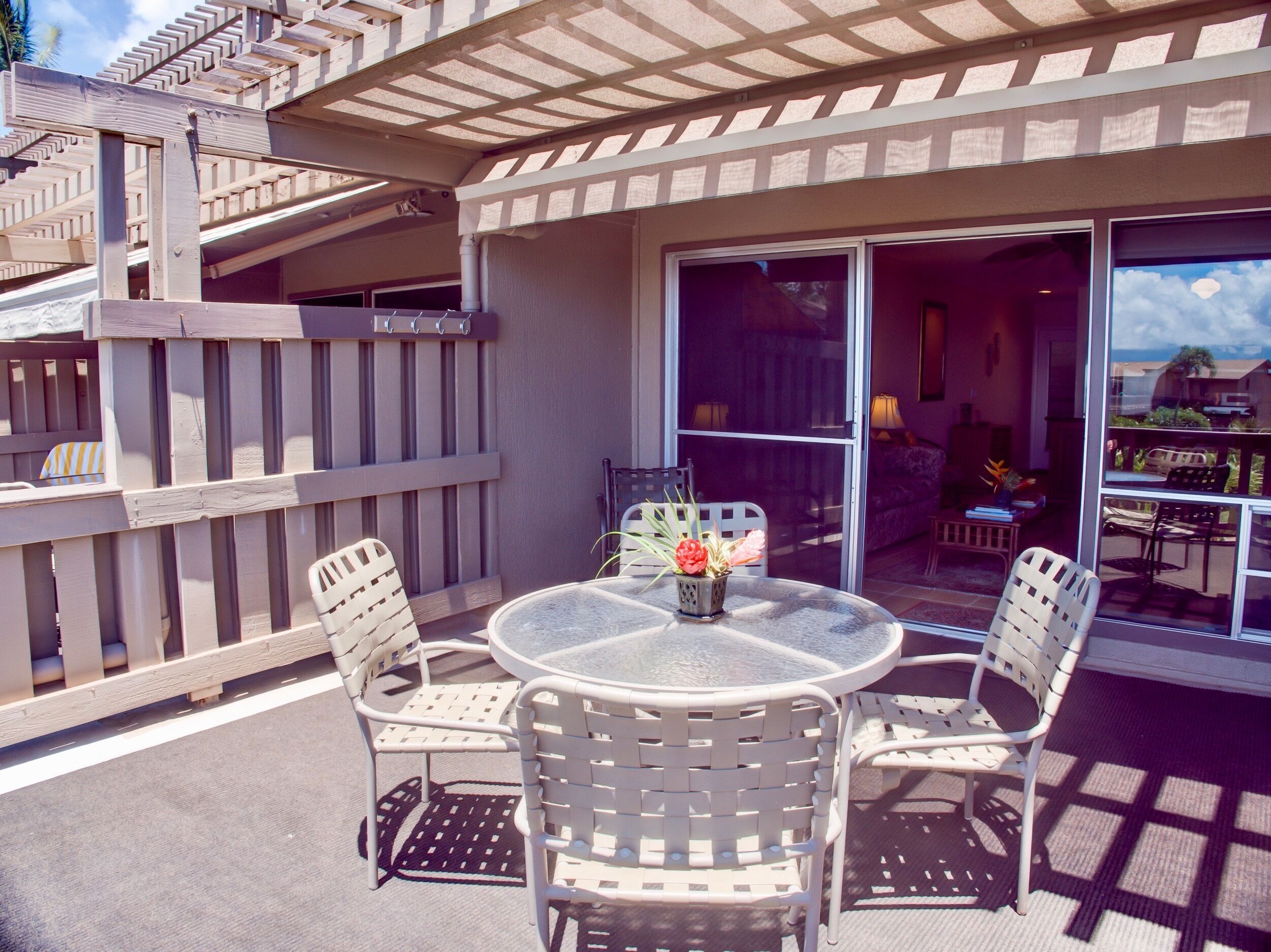 Eine Terrasse mit rundem Tisch und vier Stühlen, einem Holzzaun und einer Glastür, die zu einem Innenbereich mit Sofa und Lampe führt.