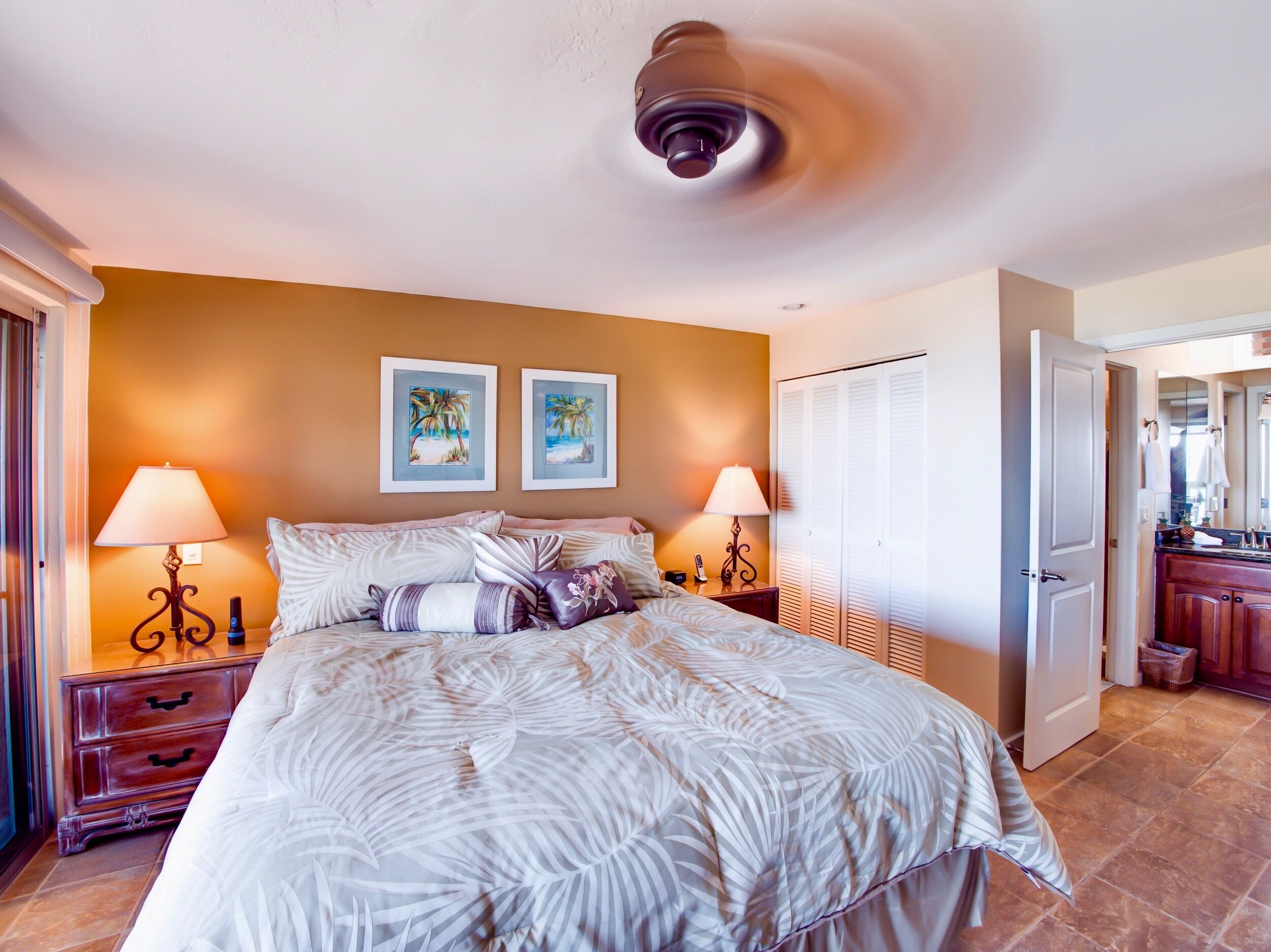 Een slaapkamer met een bed, twee bedlampen, een nachtkastje, een deur en een zichtbare badkamer door een open deur.