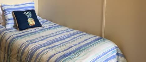 A single bed with a striped bedspread, a pineapple pillow, and a TV mounted on the wall.