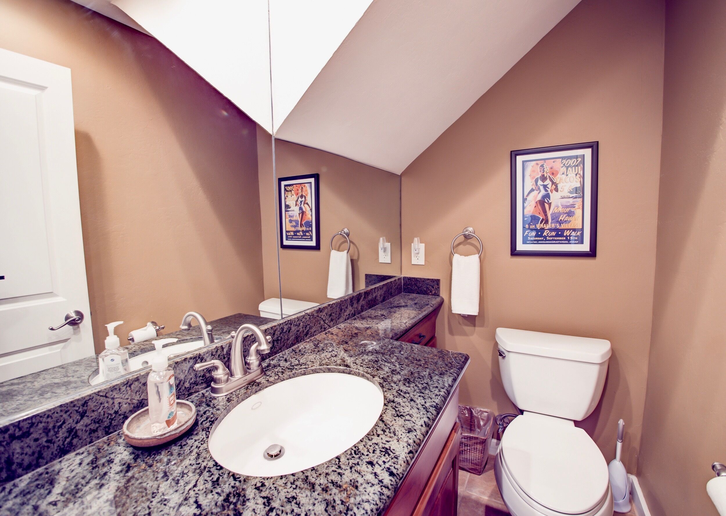 A bathroom with a granite countertop, white sink, and toilet. There are two framed posters on the wall and a towel ring with a white towel.