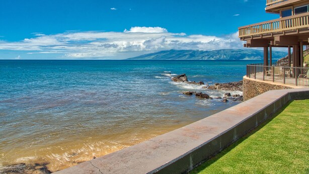 Un hotel frente al mar con balcón, un sendero de piedra y una zona ajardinada.