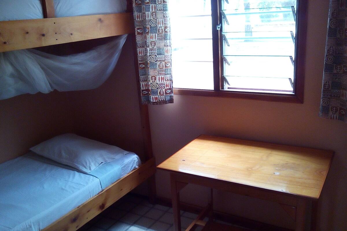 A small, single-bunk room with a wooden desk and a window.