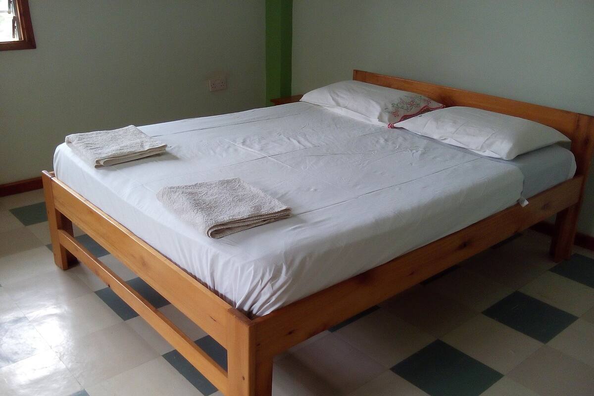 A wooden bed with white linens and a folded towel on the side.