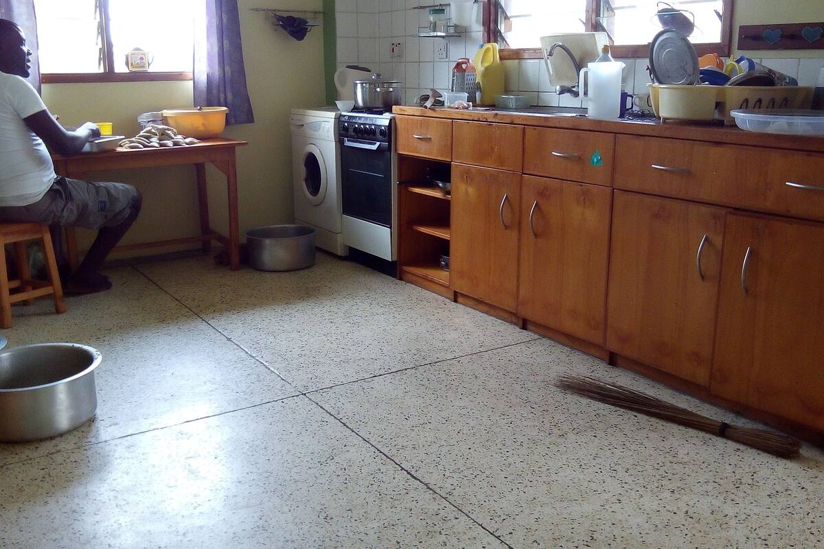 A kitchen with a washing machine, wooden cabinets, and a person sitting at a table.