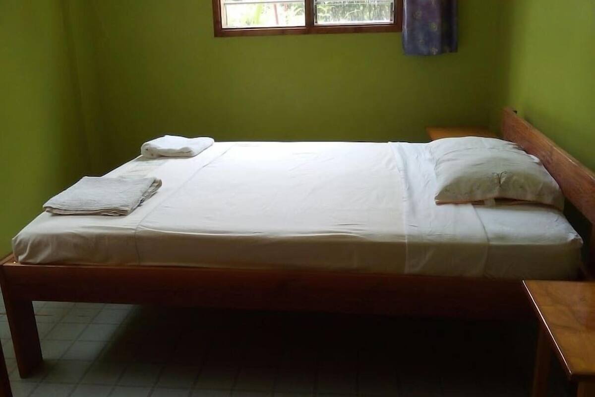 A single bed with white linens in a room with green walls and a window.