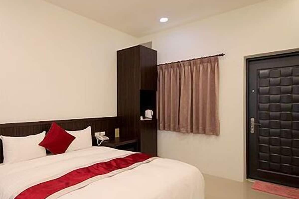A hotel room with a large bed, a bedside table with a phone, a dark door, and a window with curtains.