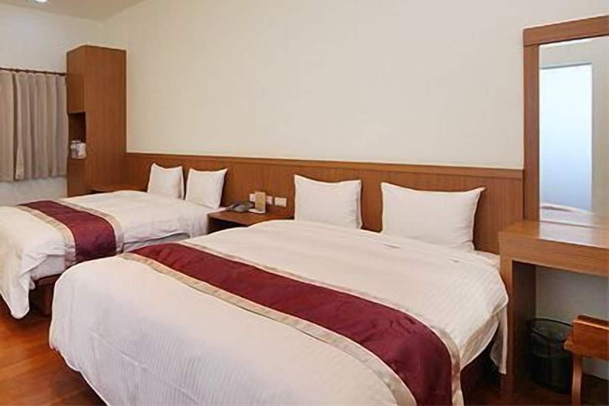 A hotel room with two beds, a wooden headboard, a bedside table, and a mirror.