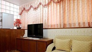 Una sala de estar con un sofá, un televisor sobre un mueble de madera y una ventana con cortinas.