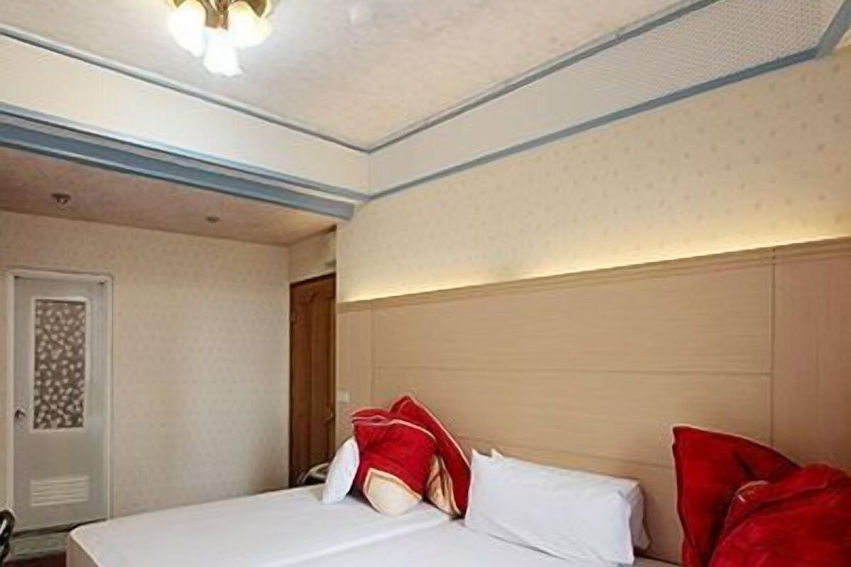 A hotel room with a large bed, two red pillows, and a white headboard.