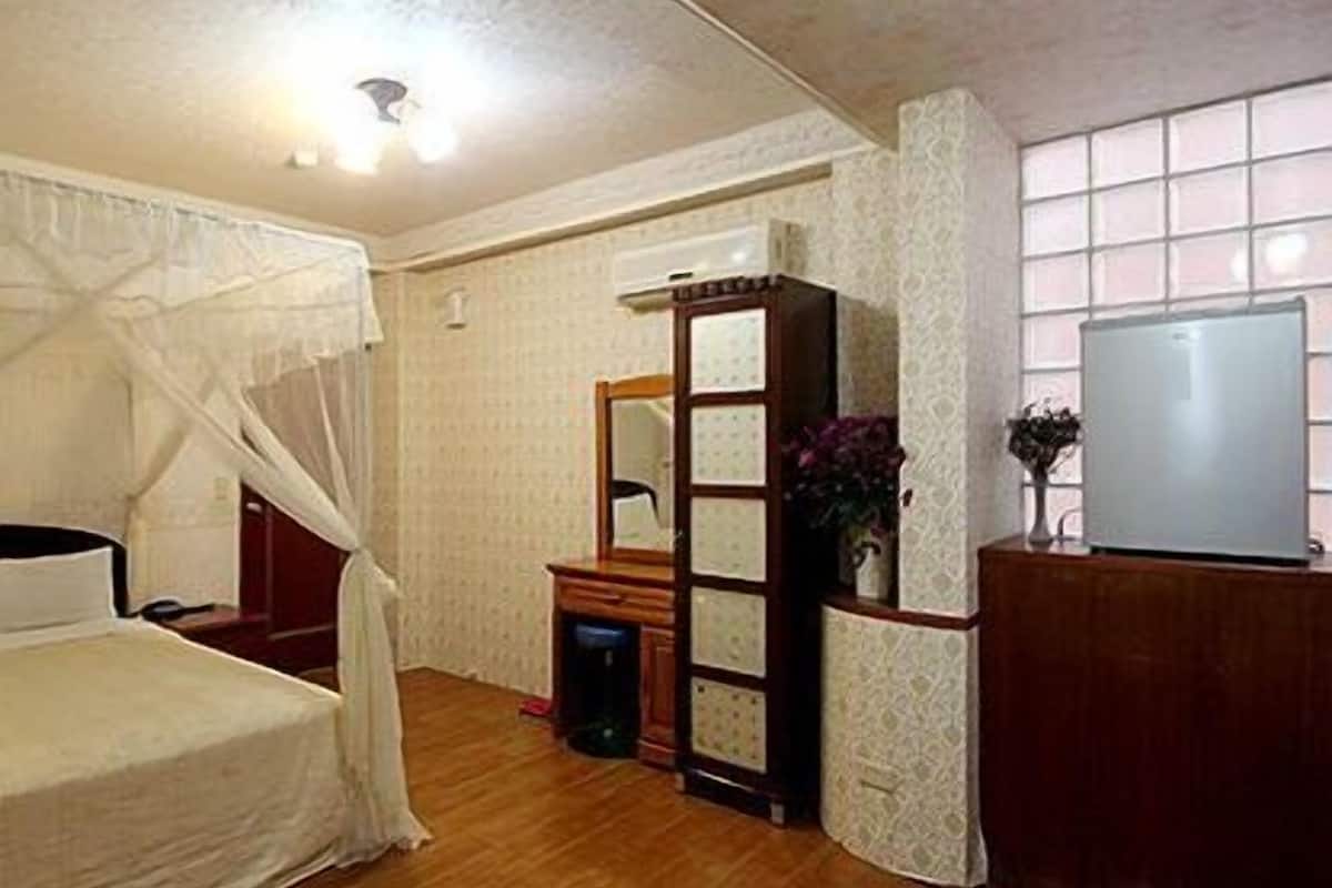 A bedroom with a bed, a wooden dresser, a mirror, and a television.