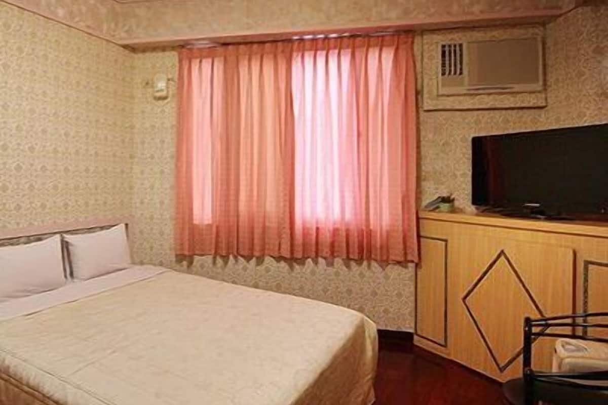 A bedroom with a bed, a desk with a television, and a chair.