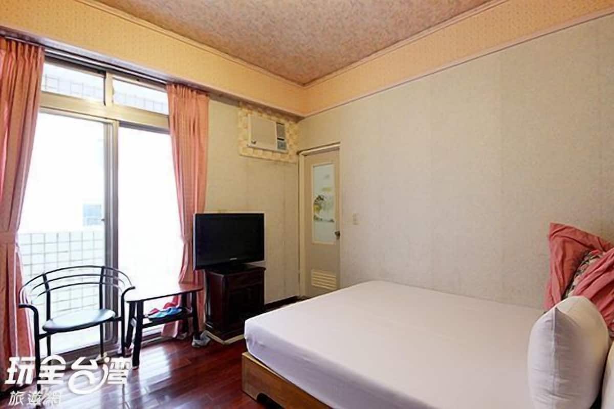 A hotel room with a bed, a television, a chair, and a window with curtains.