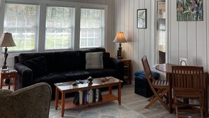 Un salon spacieux avec un canapé noir, une table basse en bois et un coin repas comprenant des chaises et une table en bois.