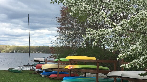 Une rangée de kayaks aux couleurs vives était alignée sur une rive herbeuse au bord d’un lac, et une jetée en bois s’étendait dans l’eau.