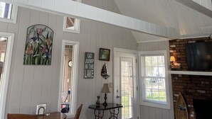 Une pièce spacieuse avec un plafond haut, un ventilateur de plafond, une cheminée, un téléviseur et un coin repas comprenant une table et des chaises.