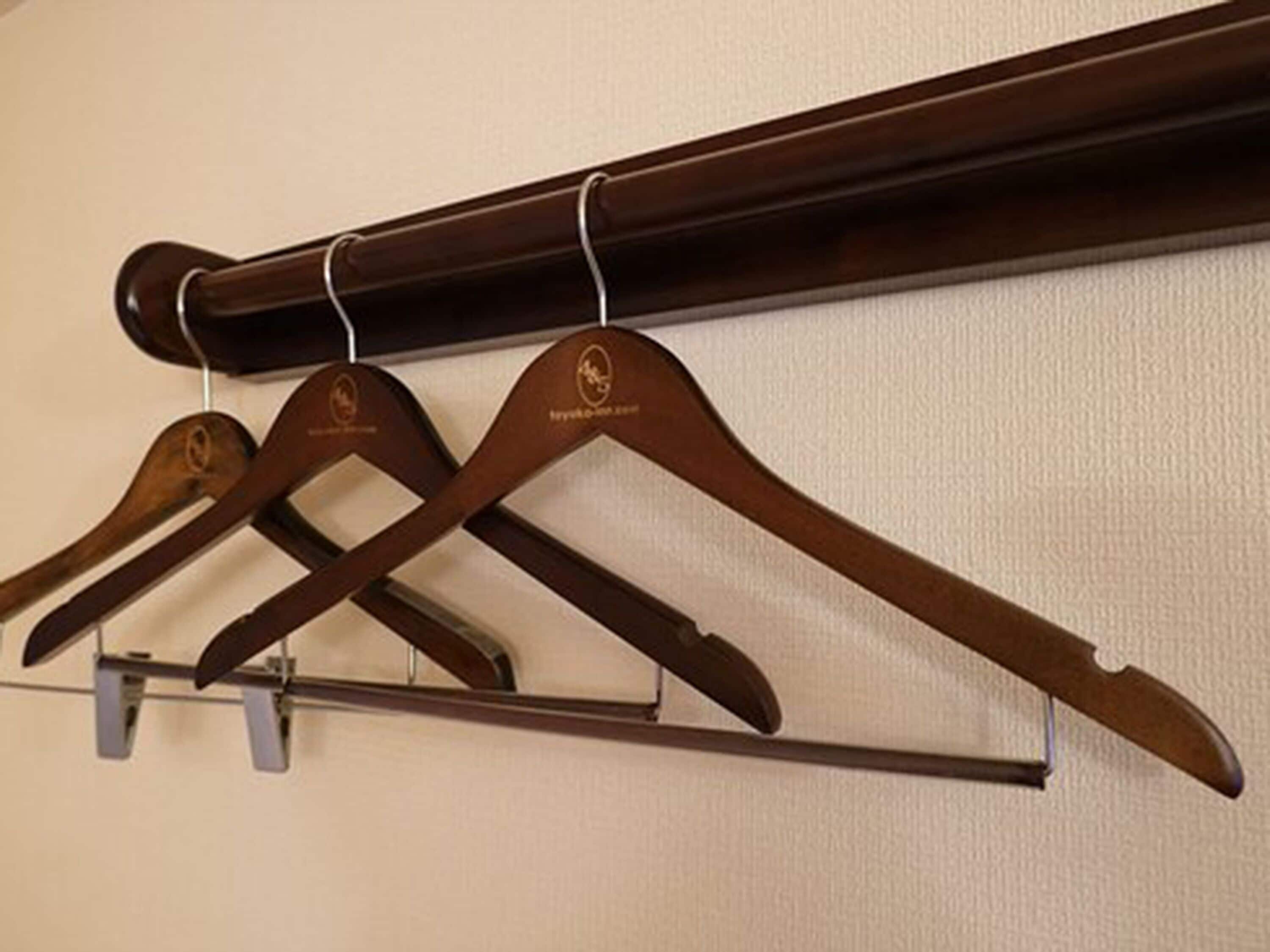 A wooden coat rack with three hangers against a textured wall.