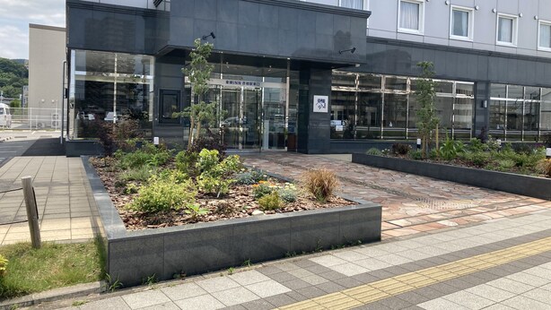 A modern building with a glass entrance, a landscaped garden area, and a paved walkway. - Toyoko Inn Hikone Station Higashi (Hikone)