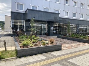 Un edificio moderno con entrada de vidrio, jardín ajardinado y un sendero pavimentado.