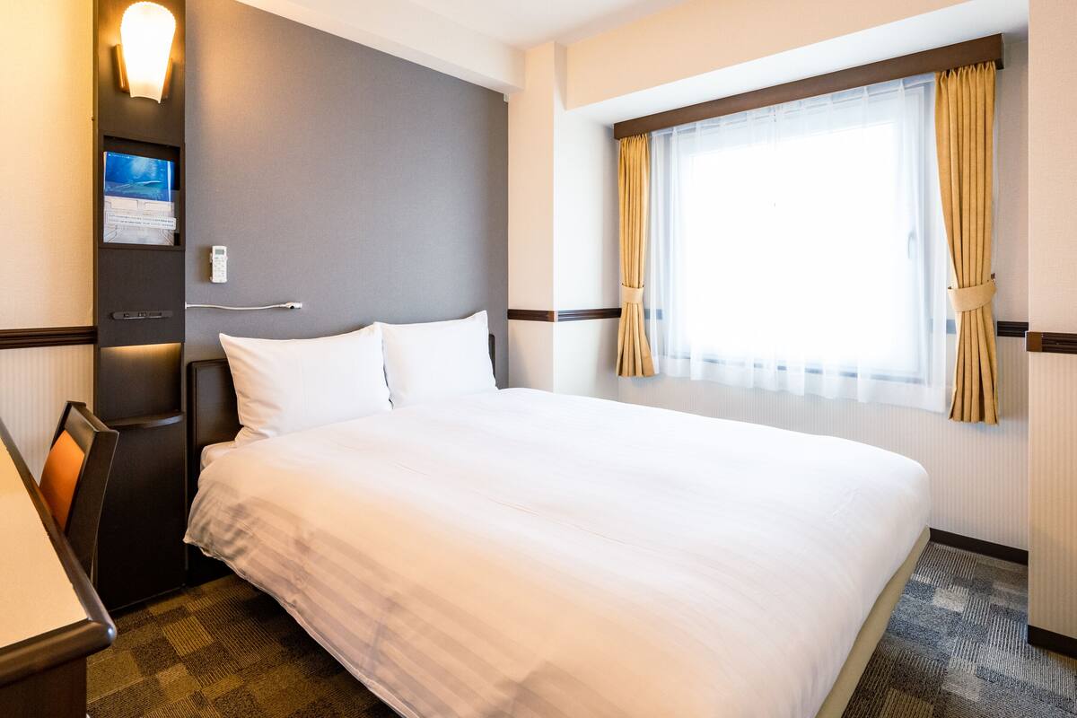 A hotel room with a large bed, a desk, a flat-screen TV, and a window with curtains.