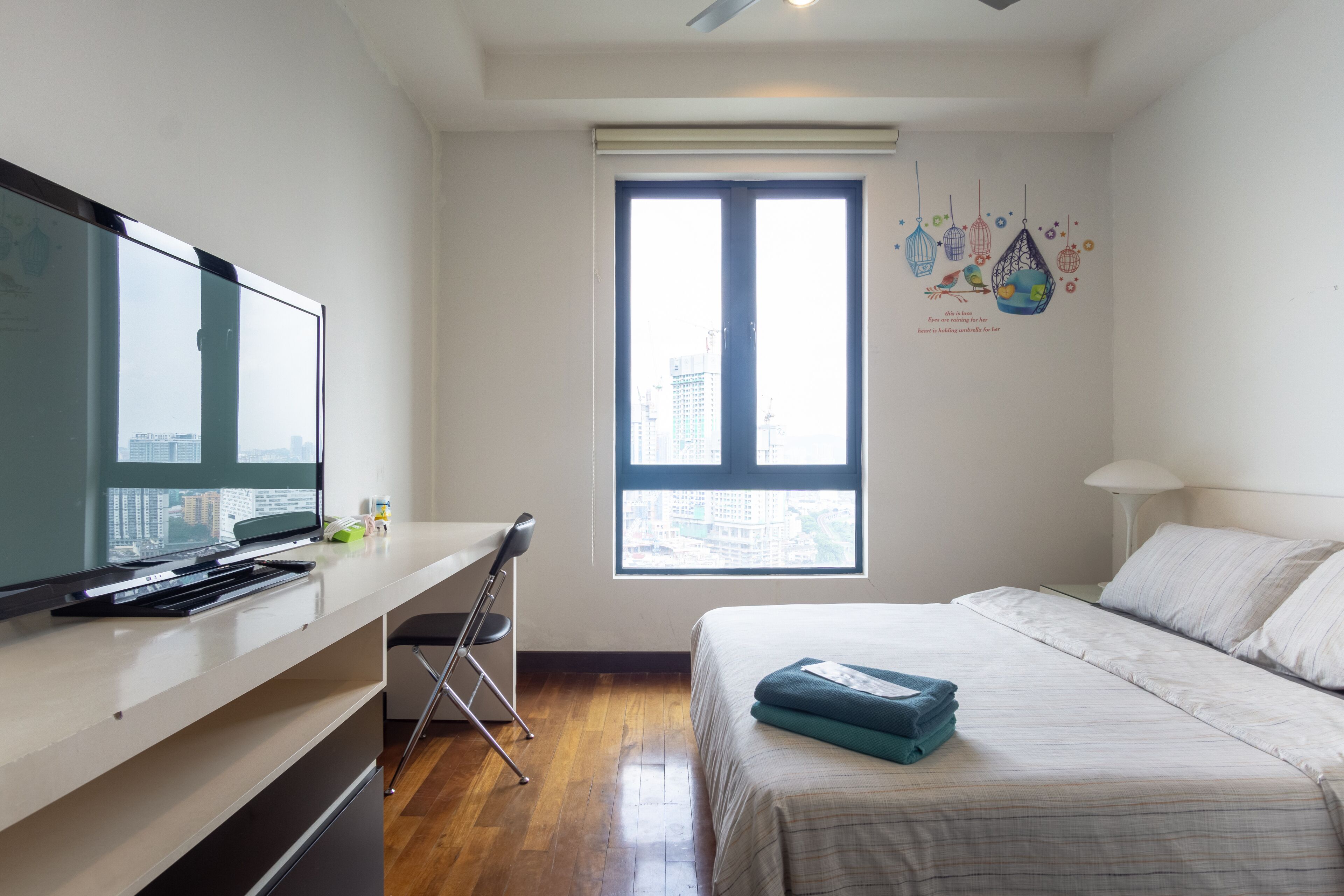 Ein modernes Hotelzimmer mit Bett, Schreibtisch mit Computer, Fenster mit Blick auf die Stadt und einer Wanddekoration.